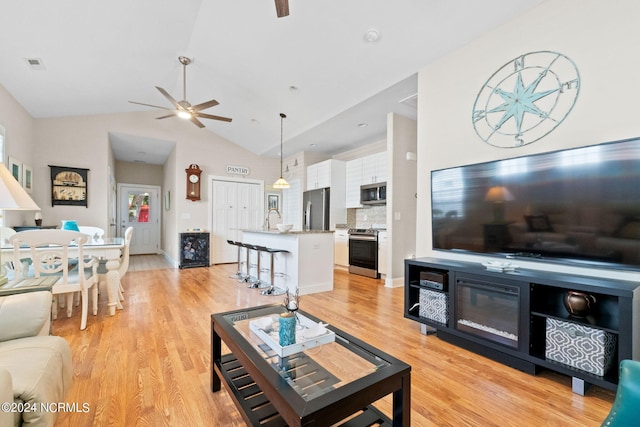 living room featuring light wood-type flooring, ceiling fan, lofted ceiling, and sink