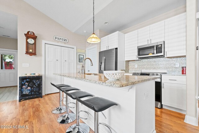 kitchen with a breakfast bar area, stainless steel appliances, white cabinetry, a sink, and light wood-type flooring