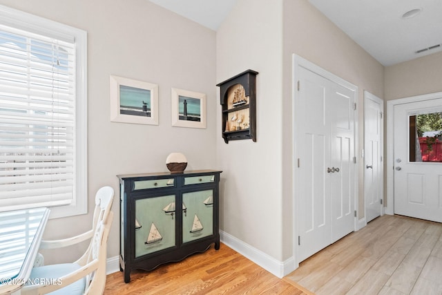 foyer entrance featuring light wood-style flooring, a healthy amount of sunlight, visible vents, and baseboards