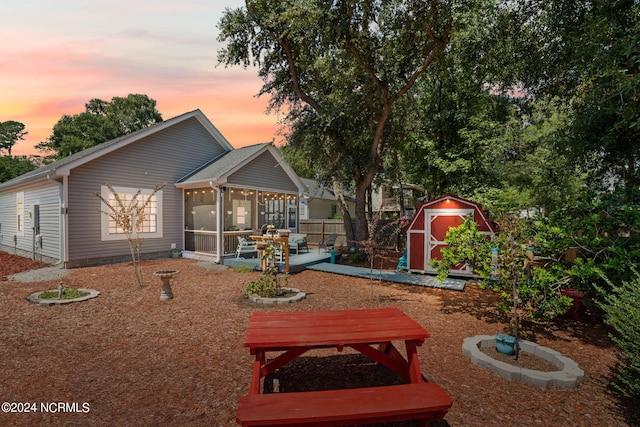 back house at dusk with a storage unit, a patio area, and a sunroom