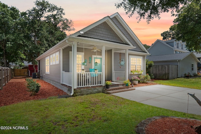 view of front of property featuring a ceiling fan, covered porch, fence, central air condition unit, and a front yard