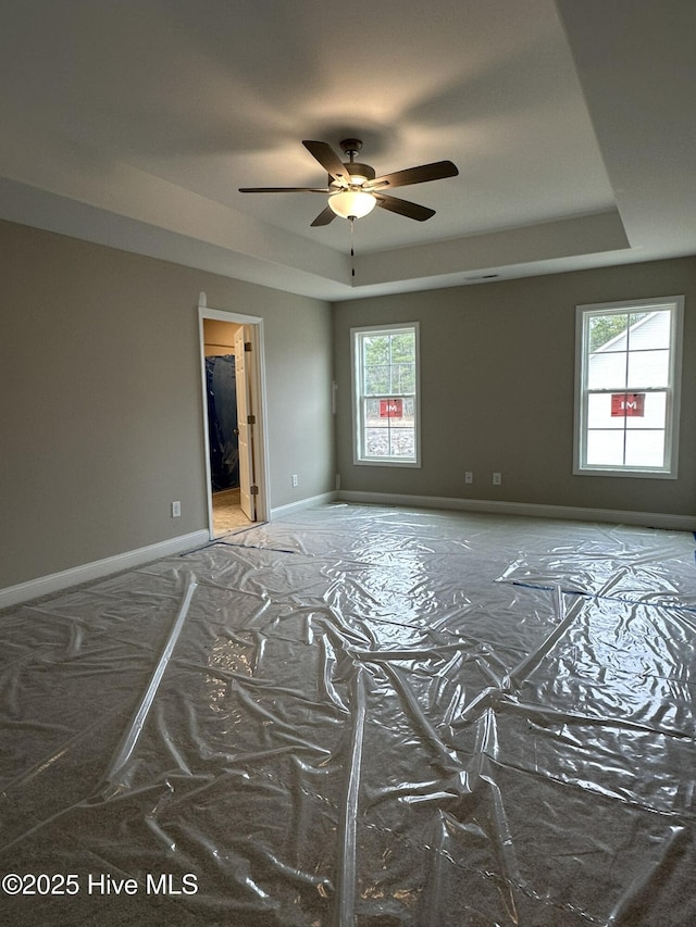 spare room featuring a tray ceiling, ceiling fan, and a healthy amount of sunlight