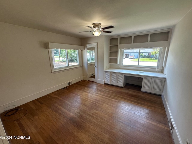 unfurnished living room with a wealth of natural light, ceiling fan, built in shelves, and dark hardwood / wood-style floors