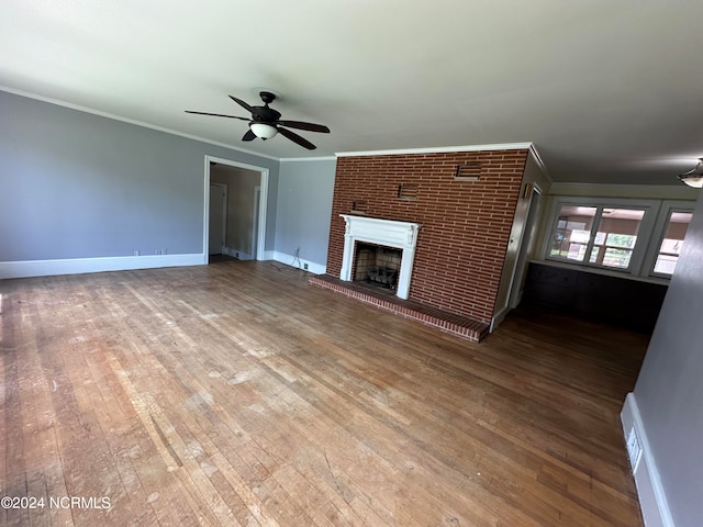 unfurnished living room featuring ornamental molding, a brick fireplace, wood-type flooring, ceiling fan, and brick wall