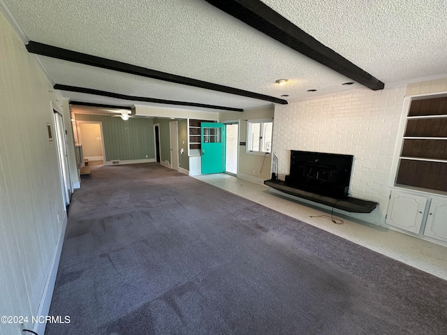 unfurnished living room with a textured ceiling, carpet flooring, beamed ceiling, and a fireplace