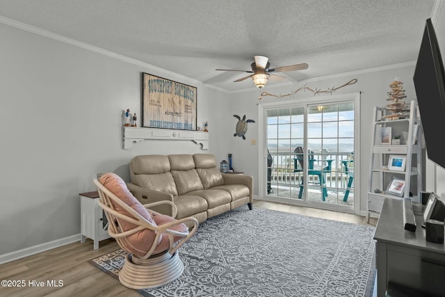 living room with a textured ceiling, light wood-style flooring, a ceiling fan, baseboards, and crown molding