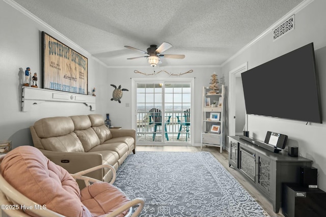 living area with a textured ceiling, a ceiling fan, visible vents, light wood finished floors, and crown molding