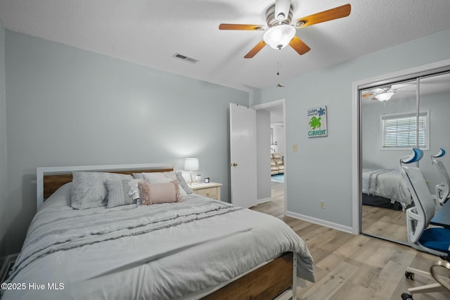 bedroom featuring light wood finished floors, visible vents, ceiling fan, a textured ceiling, and a closet