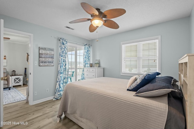 bedroom featuring a textured ceiling, a ceiling fan, visible vents, baseboards, and light wood finished floors