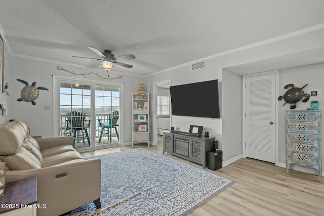 living area featuring visible vents, ceiling fan, ornamental molding, a textured ceiling, and light wood-type flooring