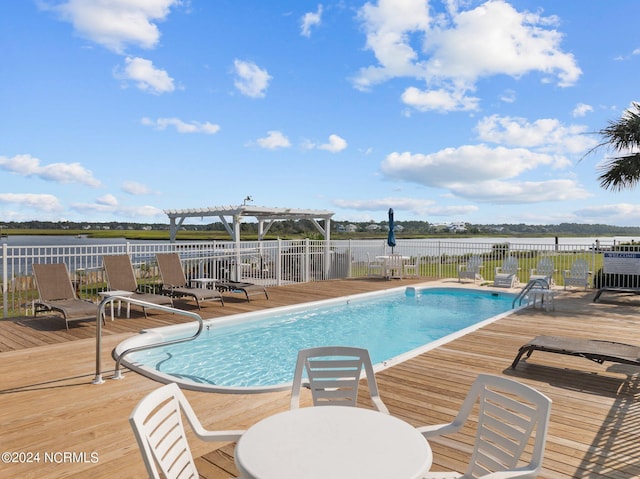 pool featuring a deck with water view, fence, and a pergola