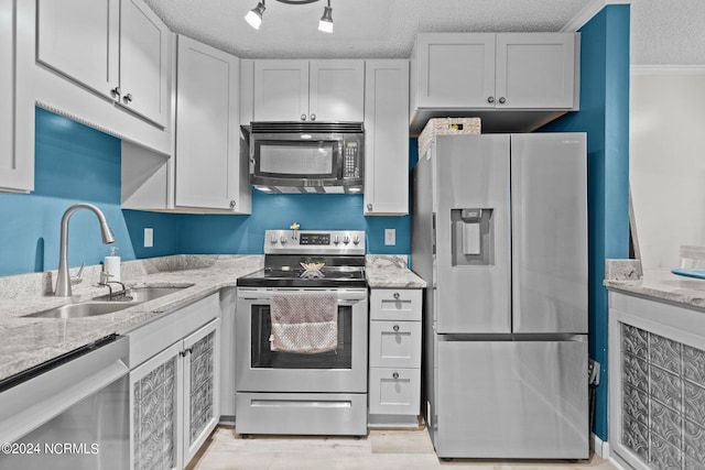 kitchen featuring a textured ceiling, light stone counters, stainless steel appliances, a sink, and crown molding