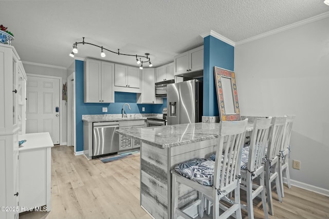 kitchen featuring light wood finished floors, appliances with stainless steel finishes, light stone counters, and ornamental molding