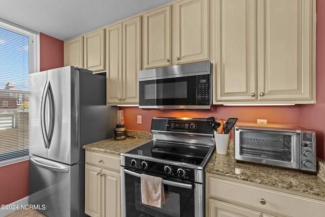 kitchen with appliances with stainless steel finishes, cream cabinets, light stone counters, and a toaster