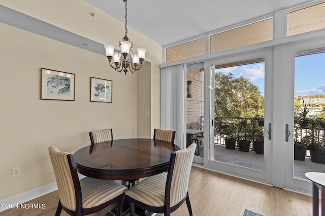 dining space featuring light wood-type flooring, baseboards, a wall of windows, and a notable chandelier