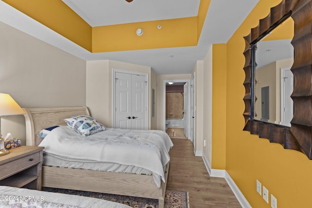 bedroom featuring a closet, connected bathroom, wood finished floors, electric panel, and baseboards