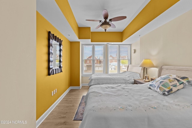 bedroom with a tray ceiling, baseboards, ceiling fan, and light wood finished floors