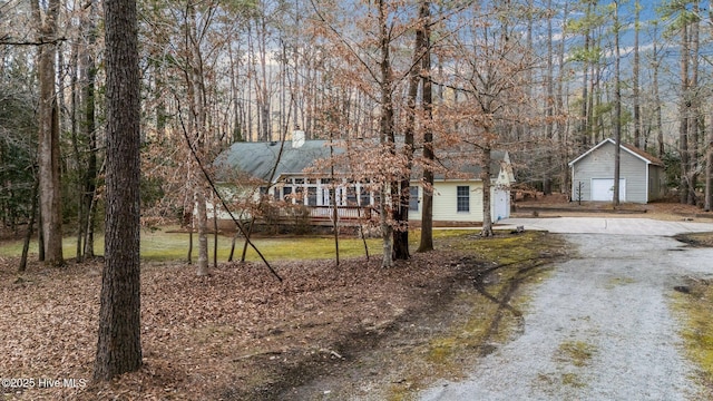 view of front of house featuring a garage, driveway, a chimney, and an outbuilding