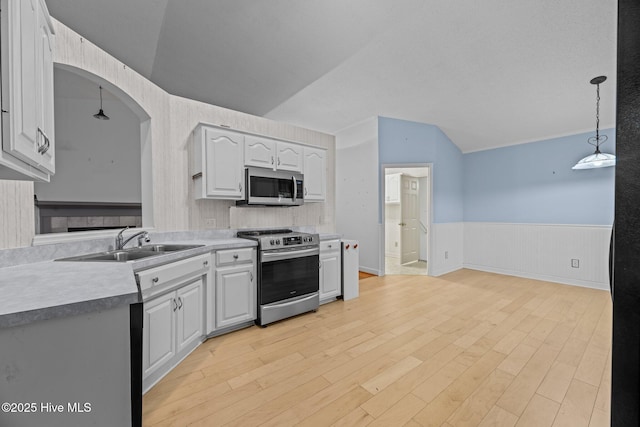 kitchen with stainless steel appliances, white cabinets, light countertops, wainscoting, and pendant lighting