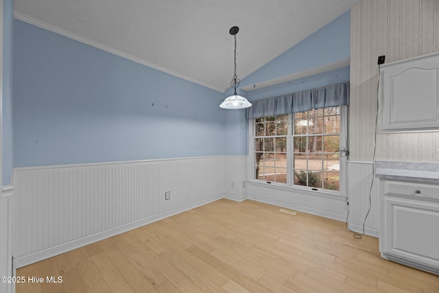 unfurnished dining area featuring a wainscoted wall, visible vents, vaulted ceiling, a textured ceiling, and light wood-type flooring