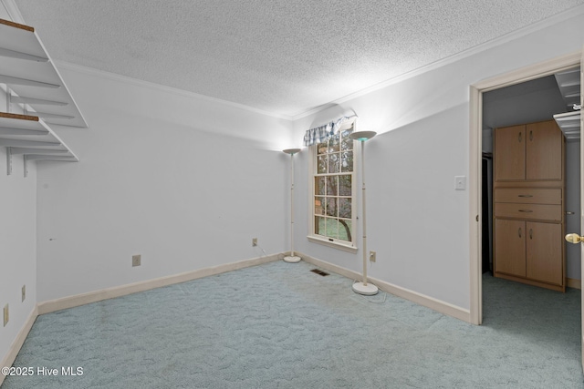 empty room with a textured ceiling, light colored carpet, visible vents, baseboards, and crown molding