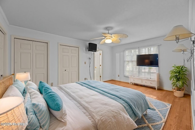 bedroom with light wood-style flooring, baseboards, ceiling fan, and multiple closets