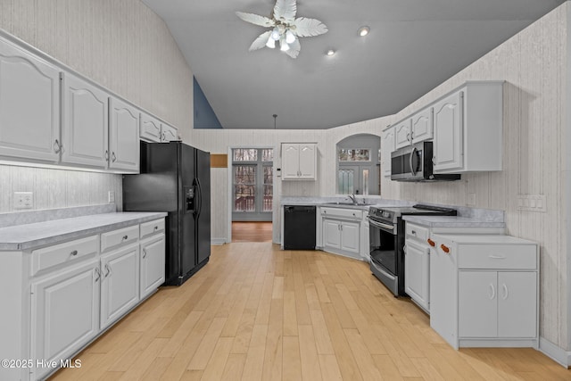 kitchen with white cabinets, light countertops, vaulted ceiling, and black appliances