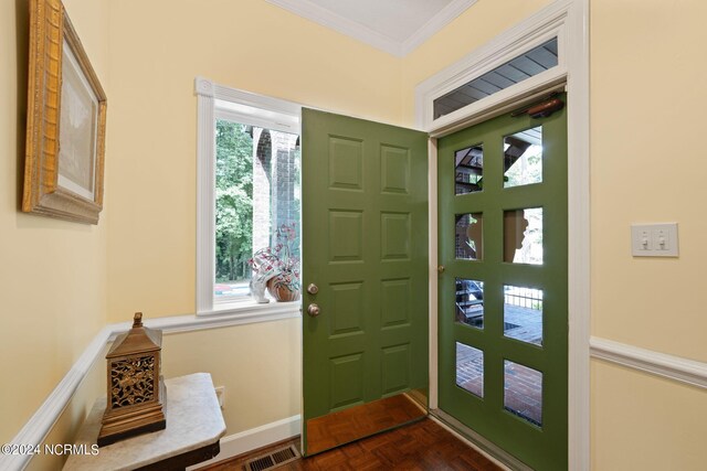 foyer entrance with ornamental molding and dark parquet flooring