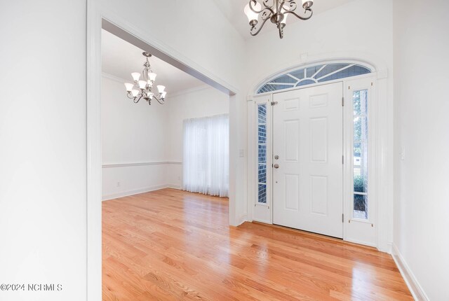 foyer entrance with ornamental molding, light hardwood / wood-style flooring, and an inviting chandelier