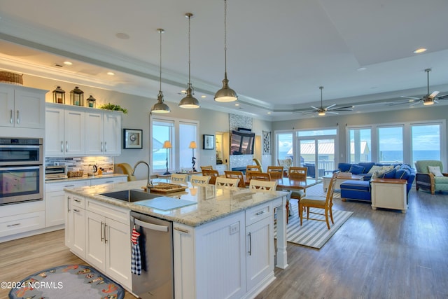 kitchen with an island with sink, stainless steel appliances, white cabinetry, and open floor plan