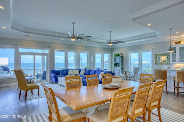 dining room with a raised ceiling, ceiling fan, wood finished floors, a water view, and recessed lighting