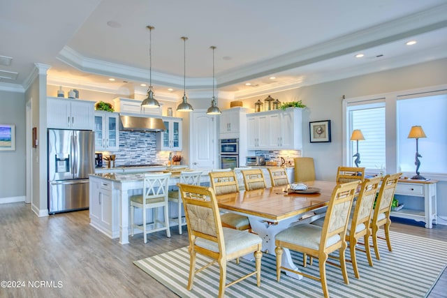 dining space with a tray ceiling, recessed lighting, light wood-style flooring, ornamental molding, and baseboards