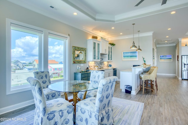 dining room with light wood-style floors, visible vents, and crown molding