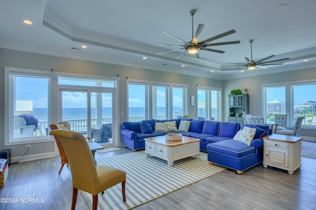 living area with a water view, light wood-type flooring, a tray ceiling, and crown molding