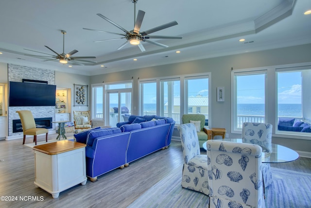 living area featuring a fireplace, recessed lighting, a raised ceiling, a water view, and light wood-style flooring