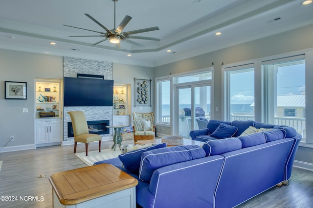 living area with a tray ceiling, a fireplace, wood finished floors, and recessed lighting