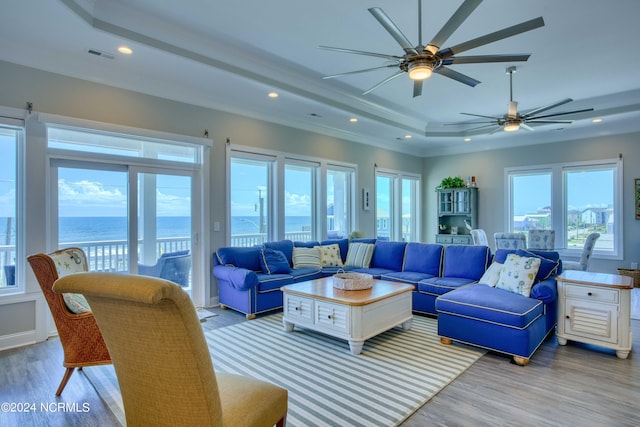 living area featuring a water view, light wood-style flooring, a tray ceiling, and recessed lighting