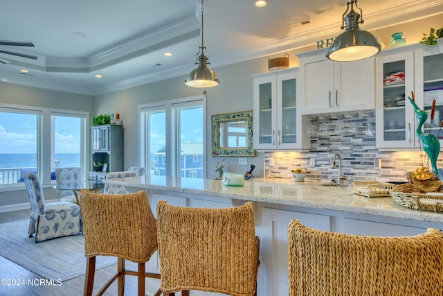 kitchen with light stone counters, a water view, glass insert cabinets, ornamental molding, and white cabinets