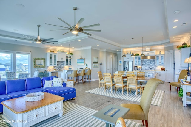 living area with baseboards, a raised ceiling, ornamental molding, light wood-type flooring, and recessed lighting