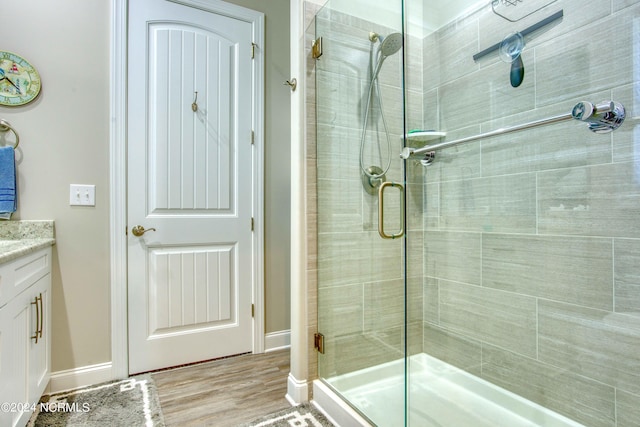 full bath with baseboards, vanity, a shower stall, and wood finished floors