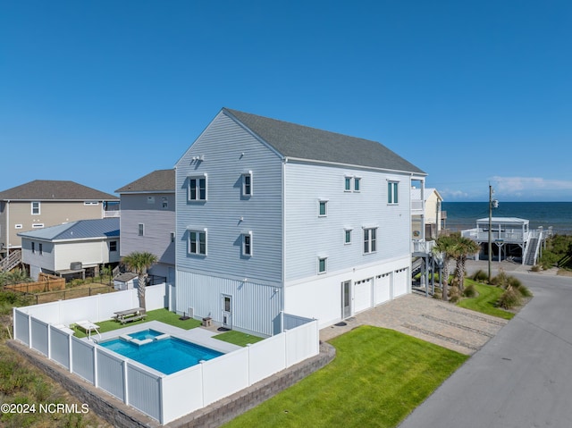 exterior space with a fenced backyard, a water view, an attached garage, a yard, and a pool with connected hot tub