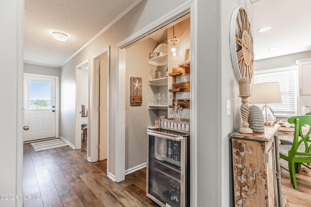 bar featuring a textured ceiling, wine cooler, hardwood / wood-style floors, crown molding, and white cabinetry