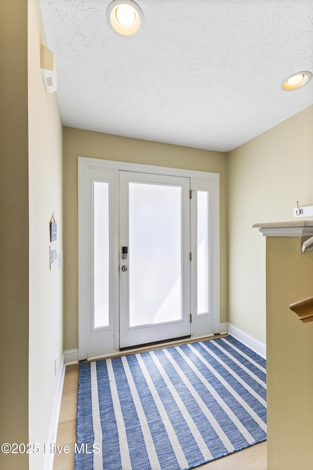 foyer entrance featuring light wood-type flooring, a textured ceiling, and baseboards