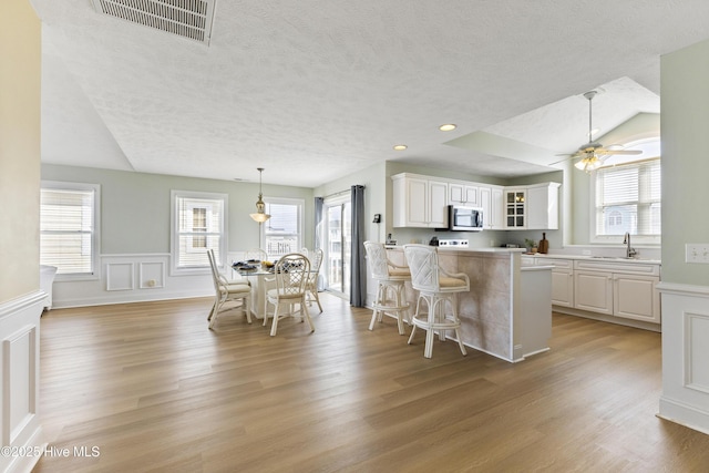 kitchen with a breakfast bar area, light countertops, stainless steel microwave, white cabinets, and a sink