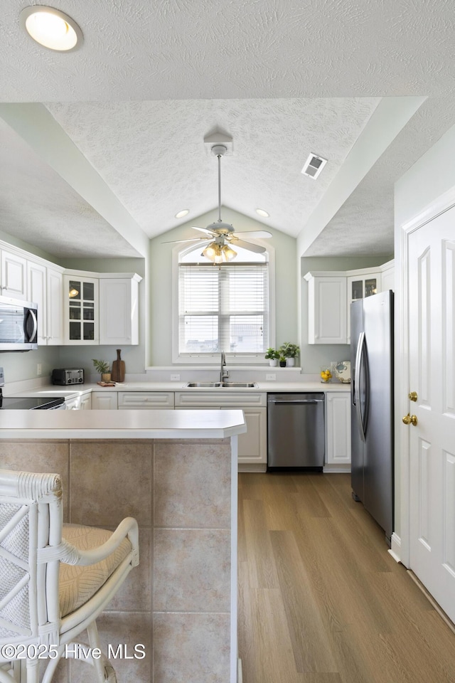 kitchen featuring stainless steel appliances, a sink, visible vents, light wood finished floors, and glass insert cabinets