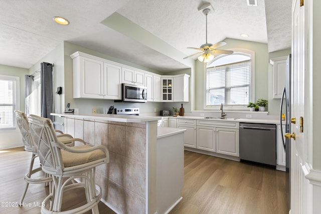 kitchen featuring a peninsula, stainless steel appliances, light wood-type flooring, white cabinetry, and a sink