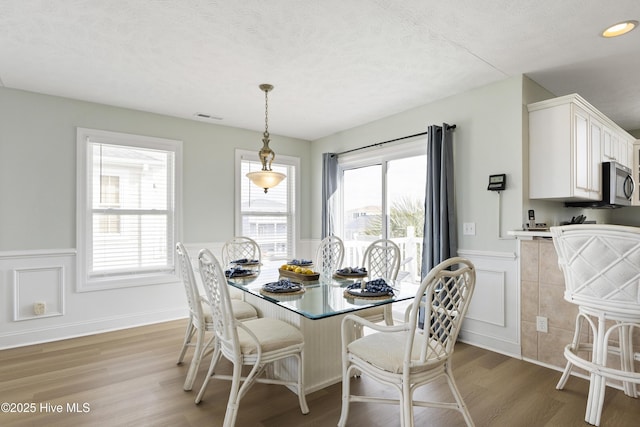 dining space featuring a wainscoted wall, light wood-style flooring, visible vents, and a textured ceiling