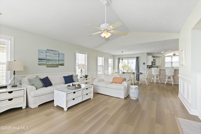 living room featuring light wood-type flooring, a wainscoted wall, ceiling fan, and lofted ceiling