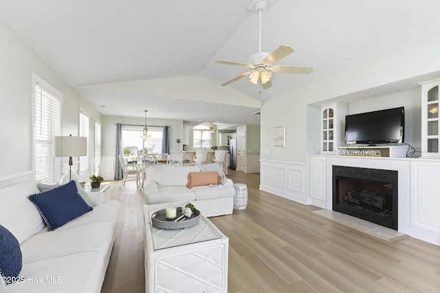 living room featuring a wainscoted wall, a fireplace, lofted ceiling, light wood-style flooring, and ceiling fan