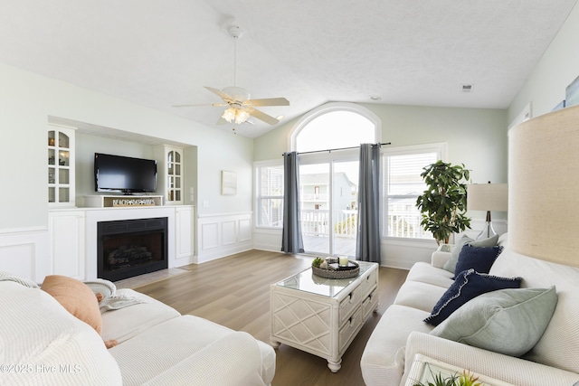 living room featuring a wainscoted wall, a fireplace with flush hearth, wood finished floors, vaulted ceiling, and a decorative wall